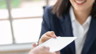 Close-up of a person in a suit handing over an envelope.