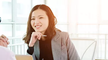 Woman in a gray blazer smiling during a meeting in a bright office.