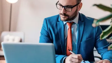 one male white collar professional looking at laptop writing