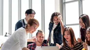 Group of people excitedly gathered around a laptop.