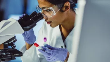 Scientist examining samples under a microscope in a lab.