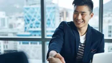 Smiling man in a suit shaking hands across a desk in an office.