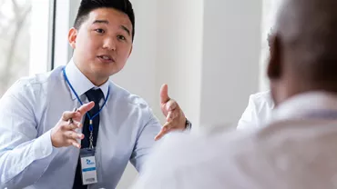 A group of diverse professionals in a meeting room, one person is speaking passionately while others listen intently.