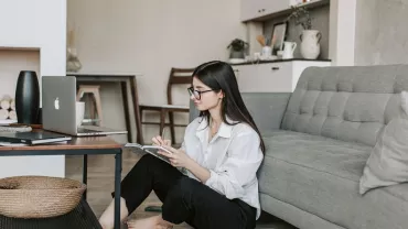 Woman sitting on floor by couch, working on laptop.