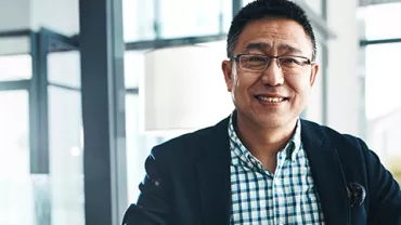 Smiling person in a checked shirt and blazer, in a bright modern office.