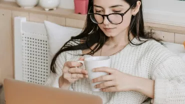 A woman holding a mug and looking at her computer screen