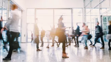 Blurry crowd of people walking through a modern office building entrance.