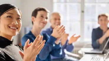 Group of people clapping during a meeting in a bright office.