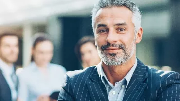 Confident man in a suit standing in front of a blurred group of professionals.