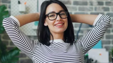 Woman in a striped shirt smiling and relaxing at her workplace.