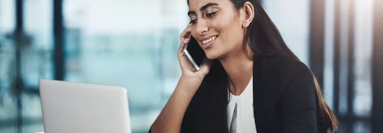 Smiling woman on a phone call while working on a laptop.